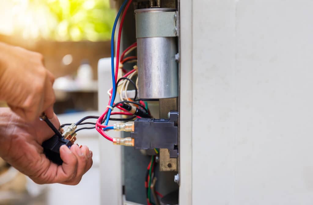Close-up of technician's hands fixing air conditioning system, changing magnetic contactor.