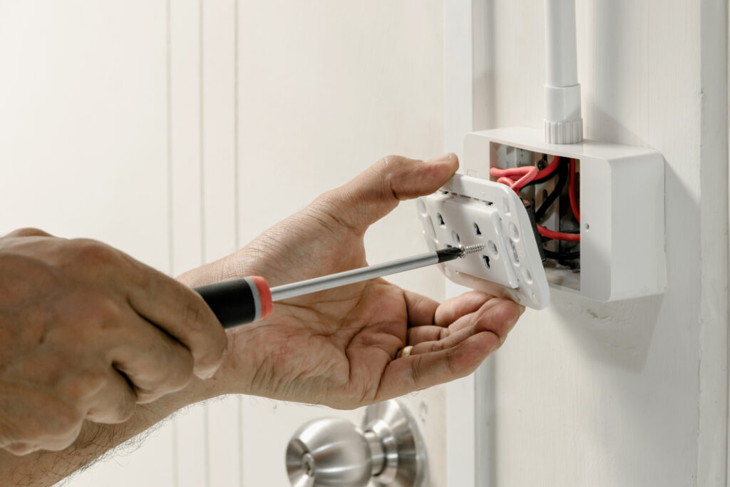 Close view of an electrician's hands as they install a GFCI outlet, using a screwdriver.