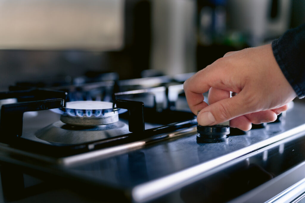 A hand turns on a stove burner fired by natural gas.