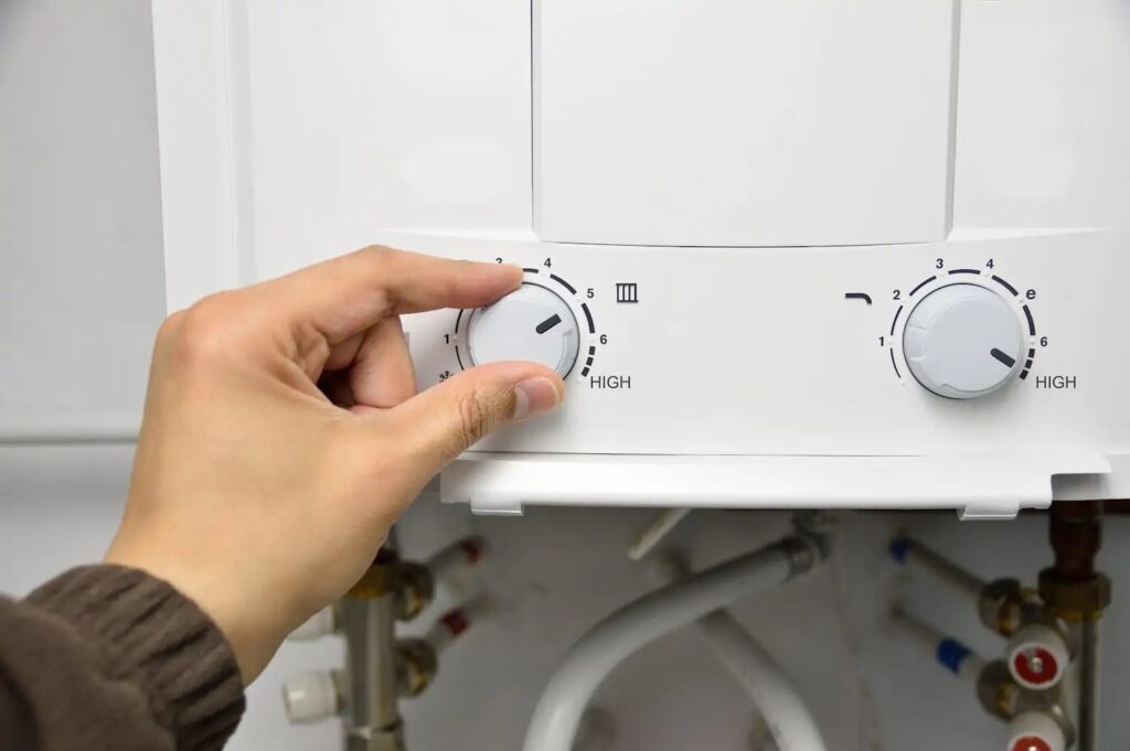 Someone's hand turning a knob on a tankless water heater.