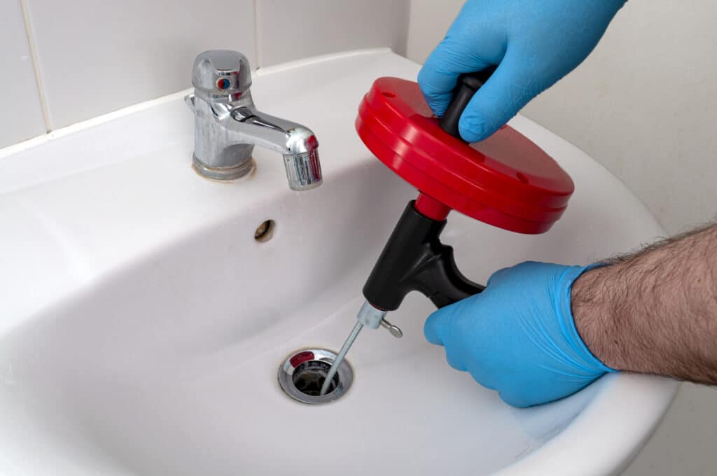 Plumber's hands using drain snake to clear a clog from a drain.