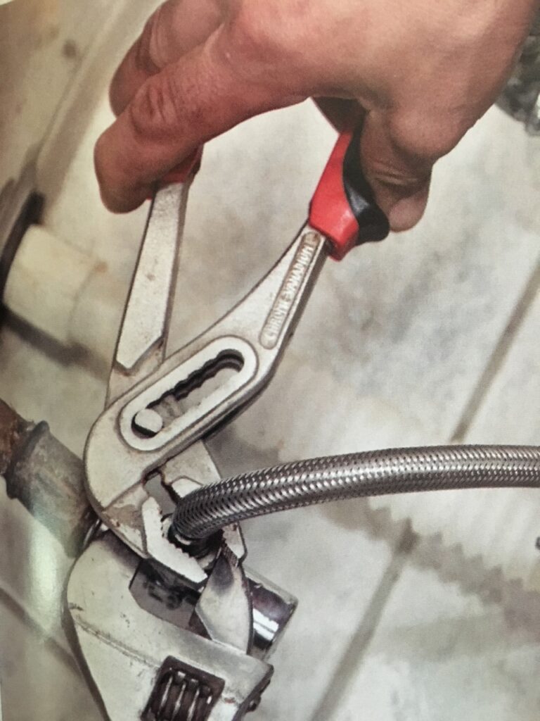 Plumber's hand using a tool to tighten a new stainless steel water hose onto an appliance.