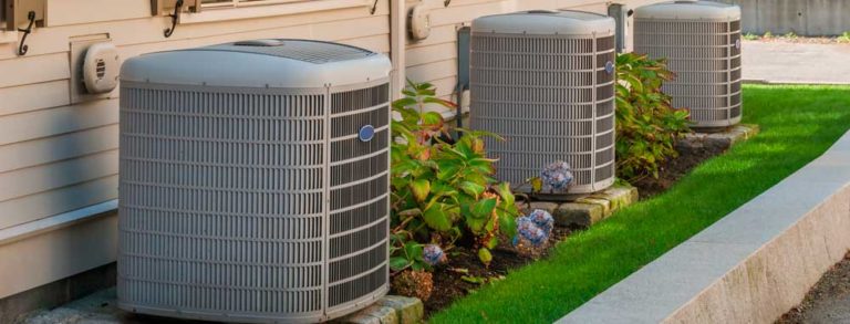 Three outdoor HVAC units next to a home, surrounded by landscaped grass and hydrangeas.