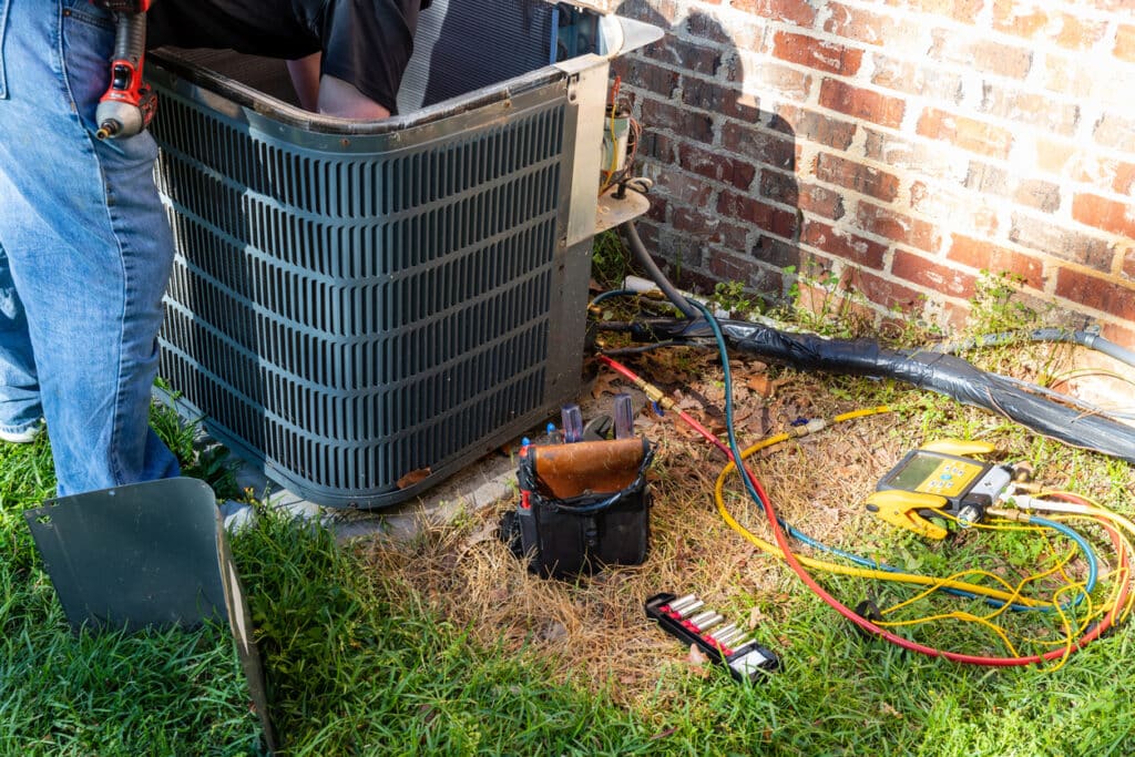 Air conditioner maintenance being performed on a system outside of a brick Baltimore home.