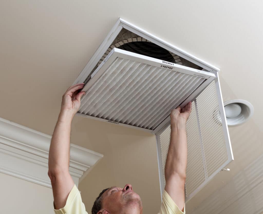 HVAC technician reaching up to open filter holder for AC filter in ceiling