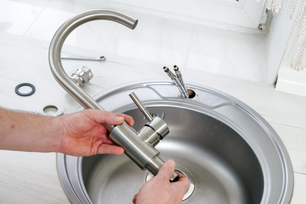 Close-up plumber hands holding a new brushed nickel faucet for installing in the bathroom sink.