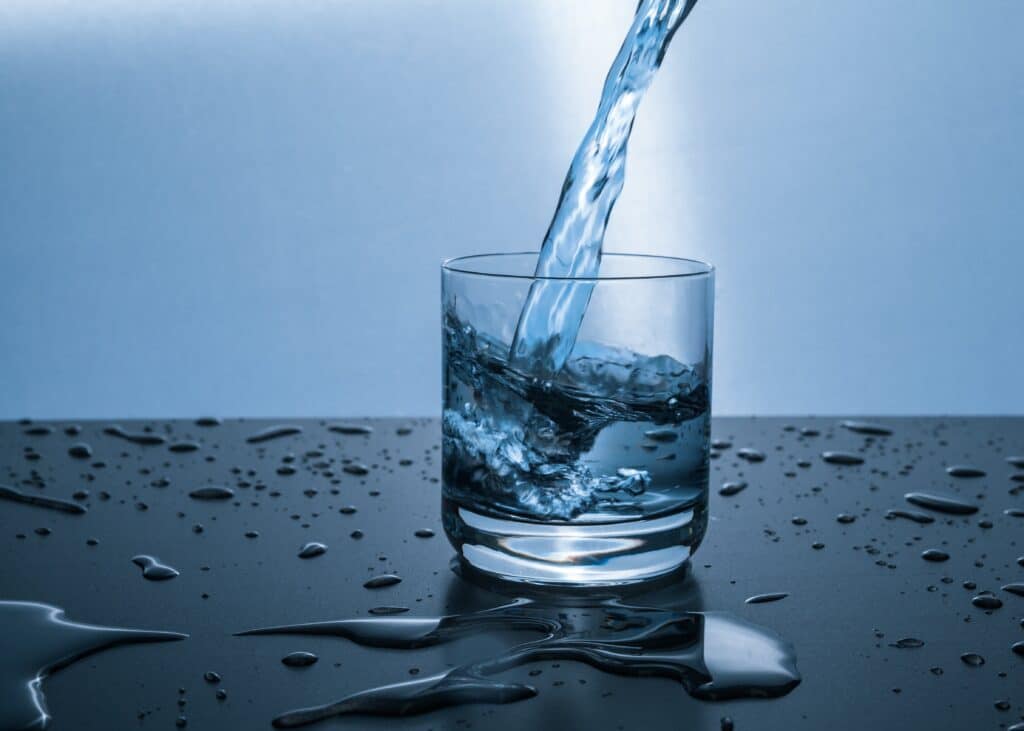Water pouring into a clear glass, which is sitting on a countertop. Blue background.