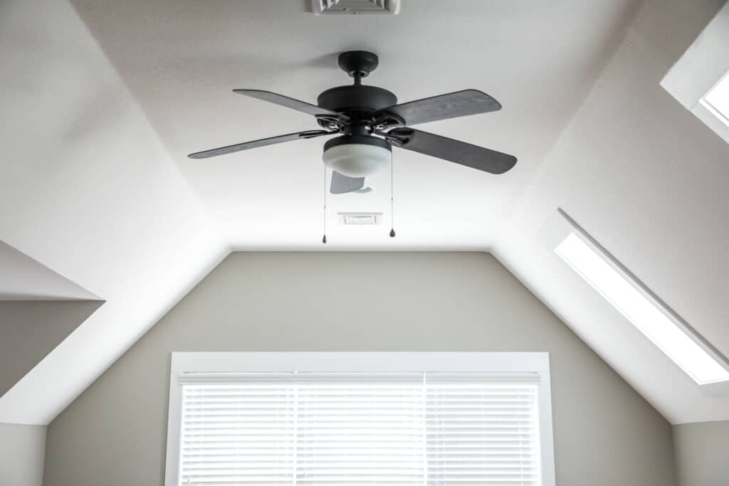 Open and airy bonus room in a new construction house with a dark wood ceiling fan, a window and blinds and white walls in background.