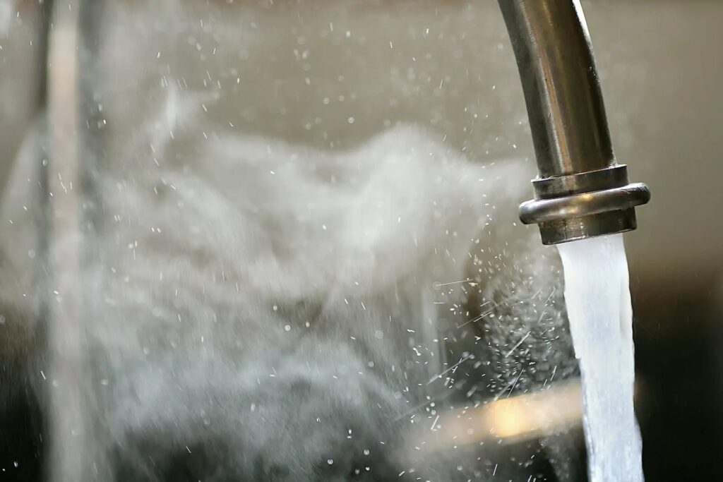 Close view of hot water flowing out of a sink, with steam around it.