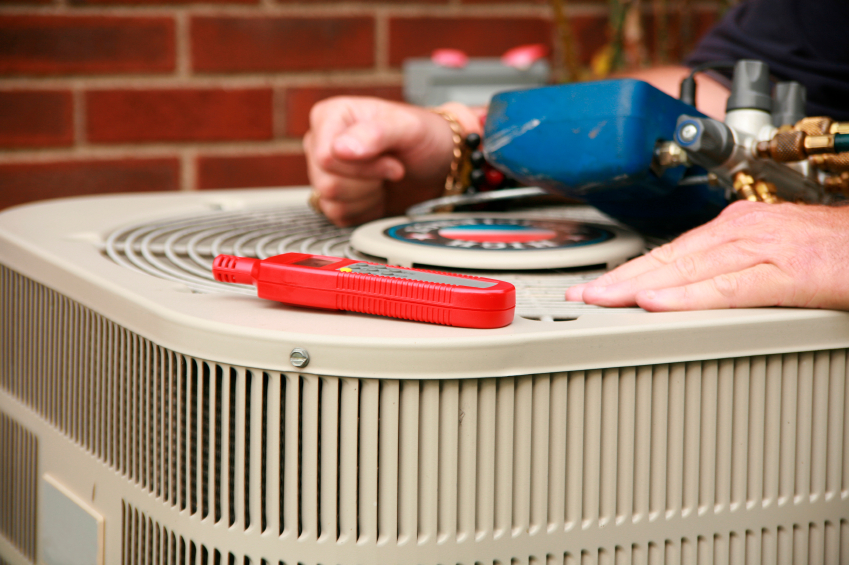 HVAC technician's hands on a heat pump next to tools.