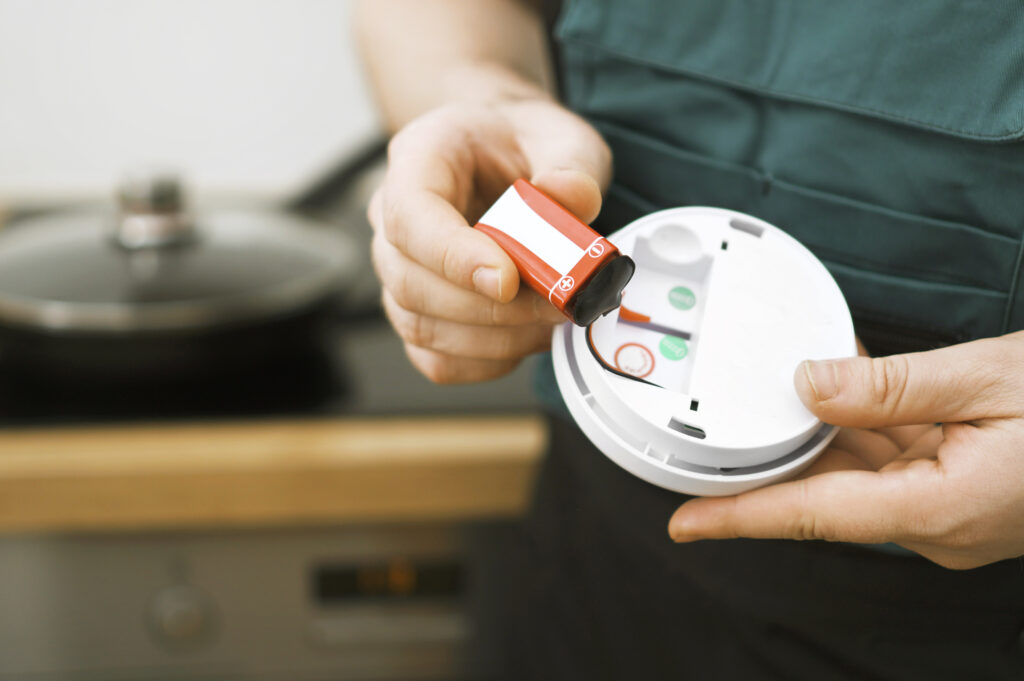 Close view of a person's hands as they change the batteries in a carbon monoxide detector