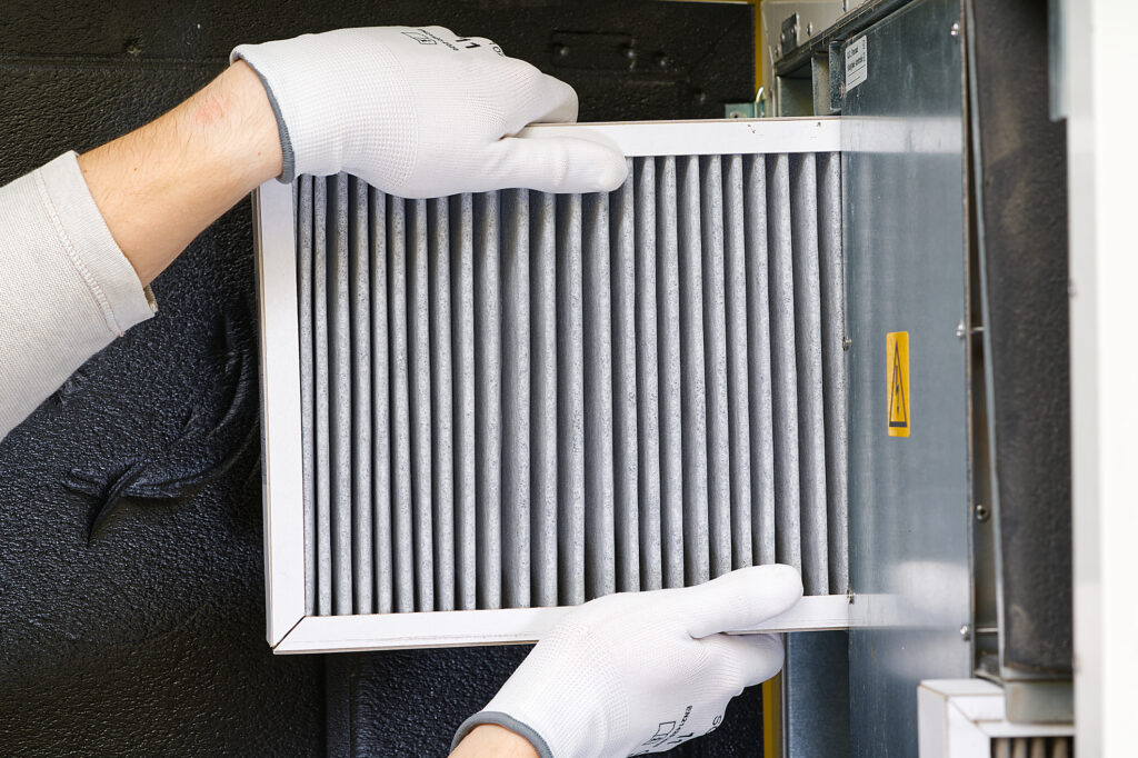 Technician's hands replacing the filter in a furnace. Replacing dirty air filter for home central air system.