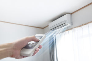 Person pointing a remote at a ductless mini-split on a wall