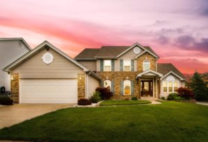 Large two-story brick-front home with lights on inside, at sunset.