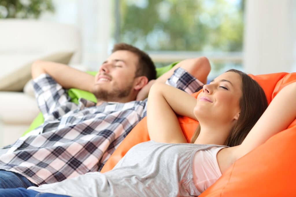 Two adults relaxing lying on comfortable pillows in the living room at home, enjoying fresh indoor air.