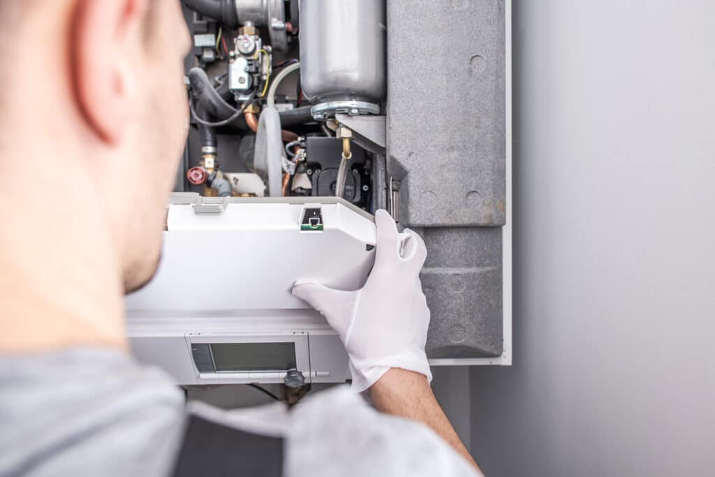Close-up of technician fixing central heating furnace system while wearing white gloves.