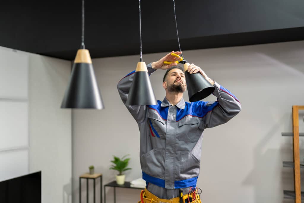 Electrician installing a black pendant light in a kitchen.