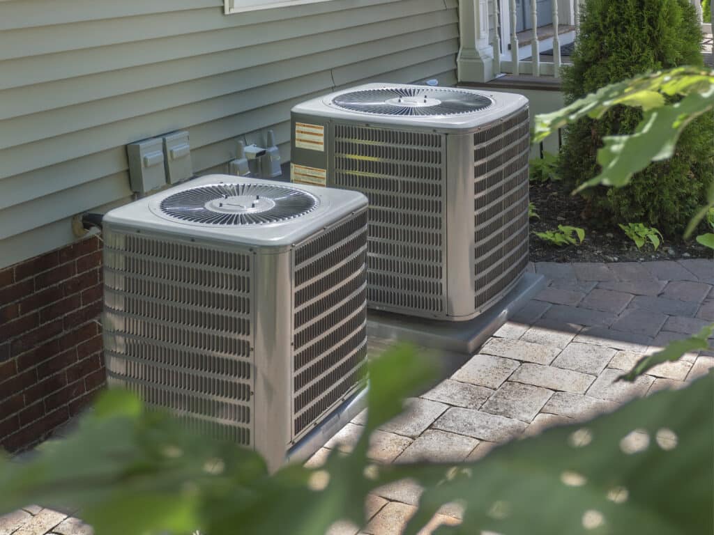 Two air conditioning units sitting on brick slab beside a Richmond, VA, home.