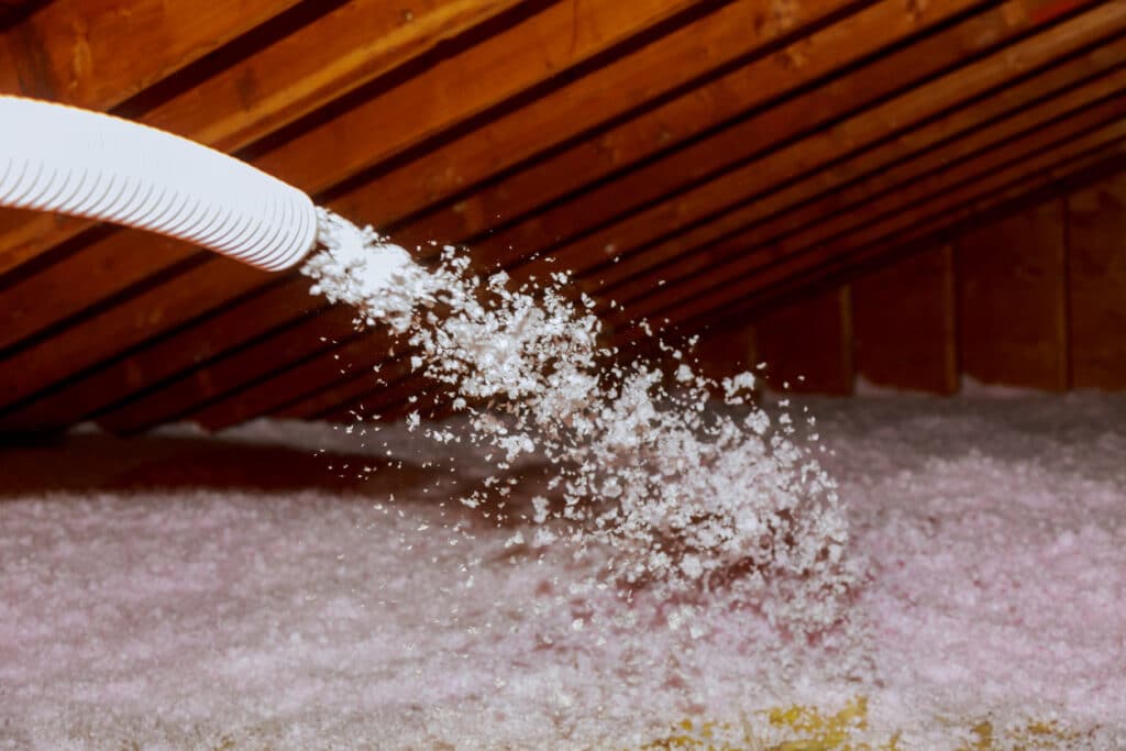 Technician blowing loose-fill insulation into an attic using plural component gun