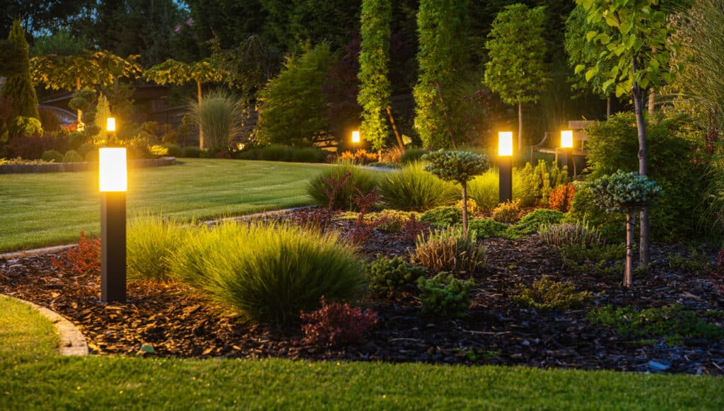 LED Light Posts Illuminating landscaped Backyard Garden During Night.