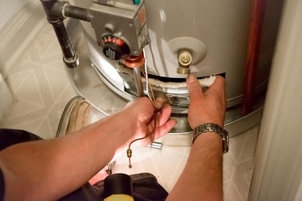 View of plumber's hands performing maintenance on a water heater.