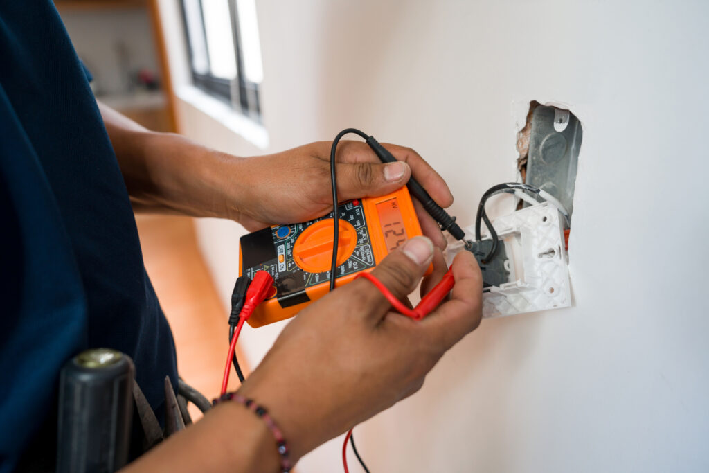Close-up on an electrician fixing an electrical outlet in a white wall and measuring the voltage.