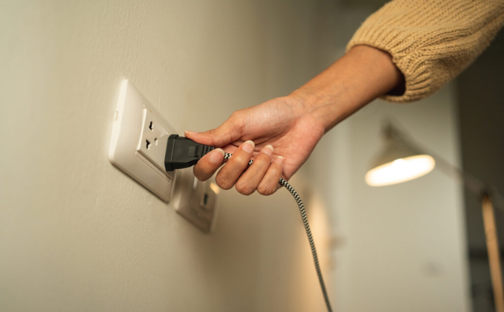 Close-up of a person's hand plugging a cable in an outlet on a white wall.