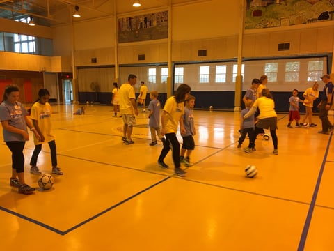 Group of kids playing soccer in a gymnasium.