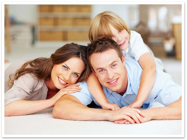 Parents and young child lying on floor together, smiling at camera.