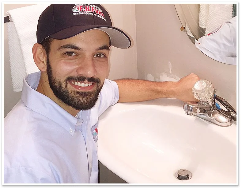 Technician smiling at camera while repairing a bathroom sink faucet.