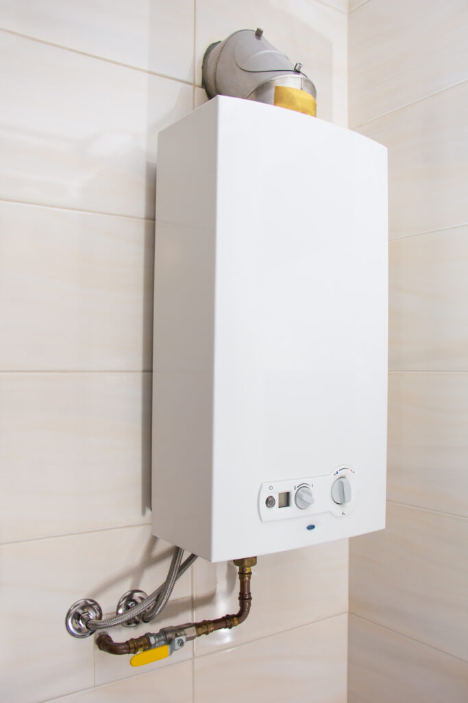 White tankless water heater installed against beige wall.